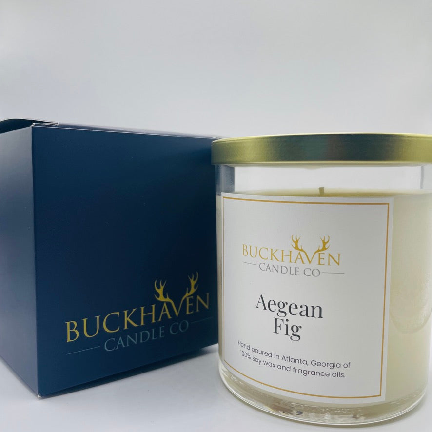 Aegean Fig candle with gold lid sitting next to display box against a white background.